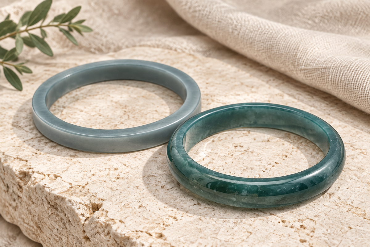 Two Guatemalan jadeite bangles inspired by current blue and grey-green catalogue pieces, arranged on neutral linen and pale stone