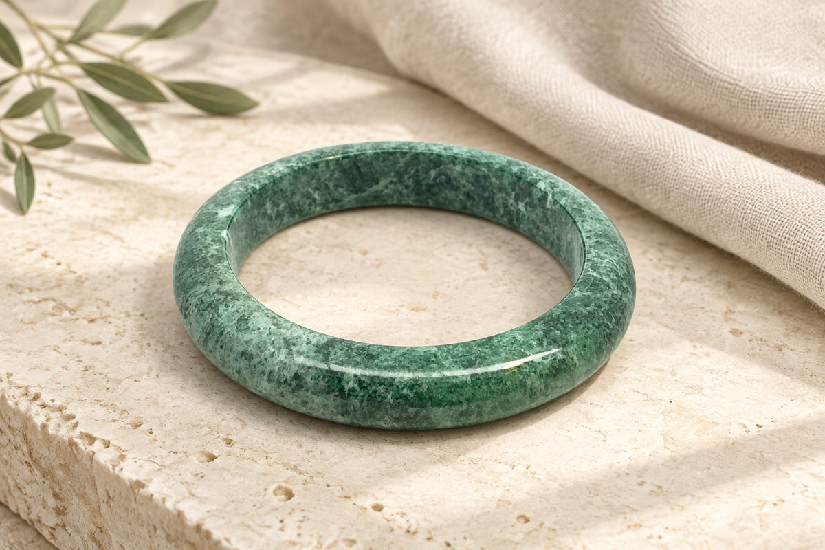 Illustrative rich mottled green Kazakh jadeite bangle inspired by an active ZHAUHAR catalogue item, styled on warm ivory limestone